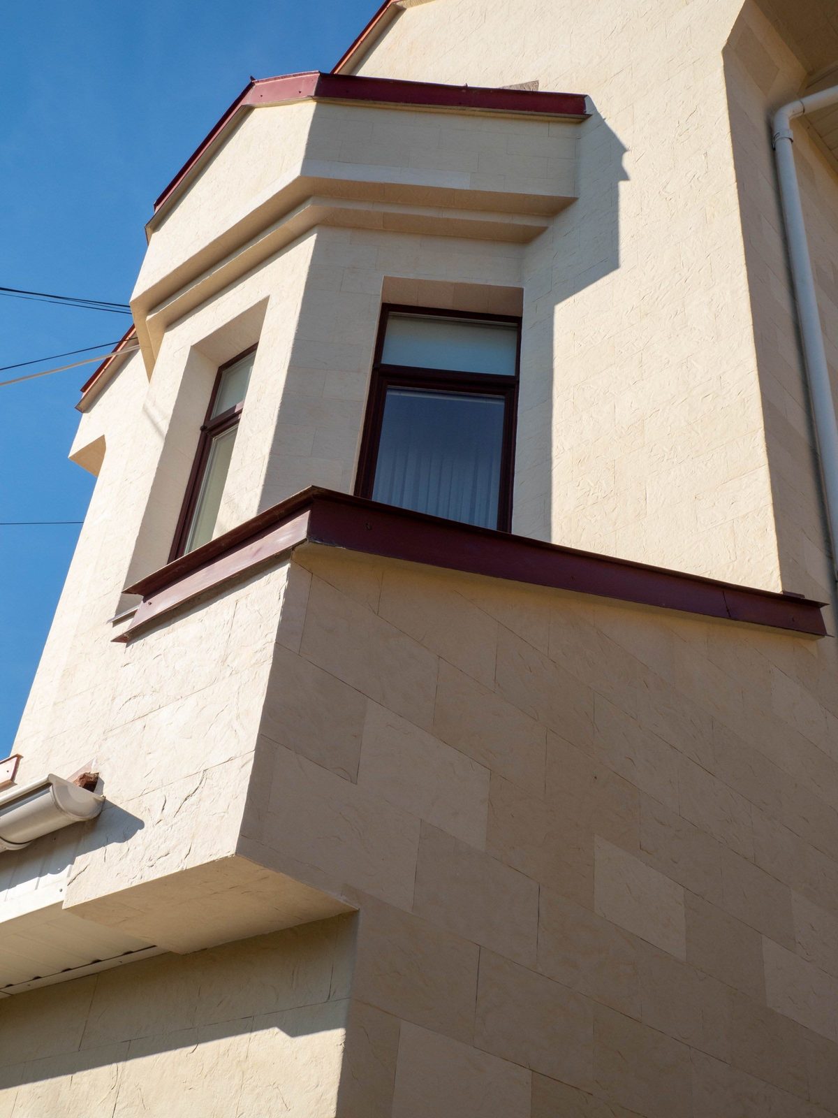 Haut pignon et bow-window vus d'en bas, pierre flexible beige et cadres de fenêtres bruns