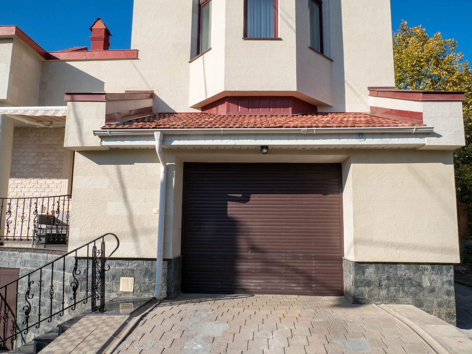 Porte de garage brune sous un pignon, façade en pierre flexible Tender Rock et allée pavée