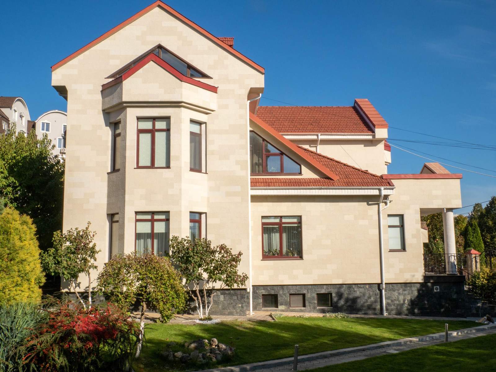 Vue générale de la maison depuis la pelouse : bow-window, pignons et toit en tuiles rouges