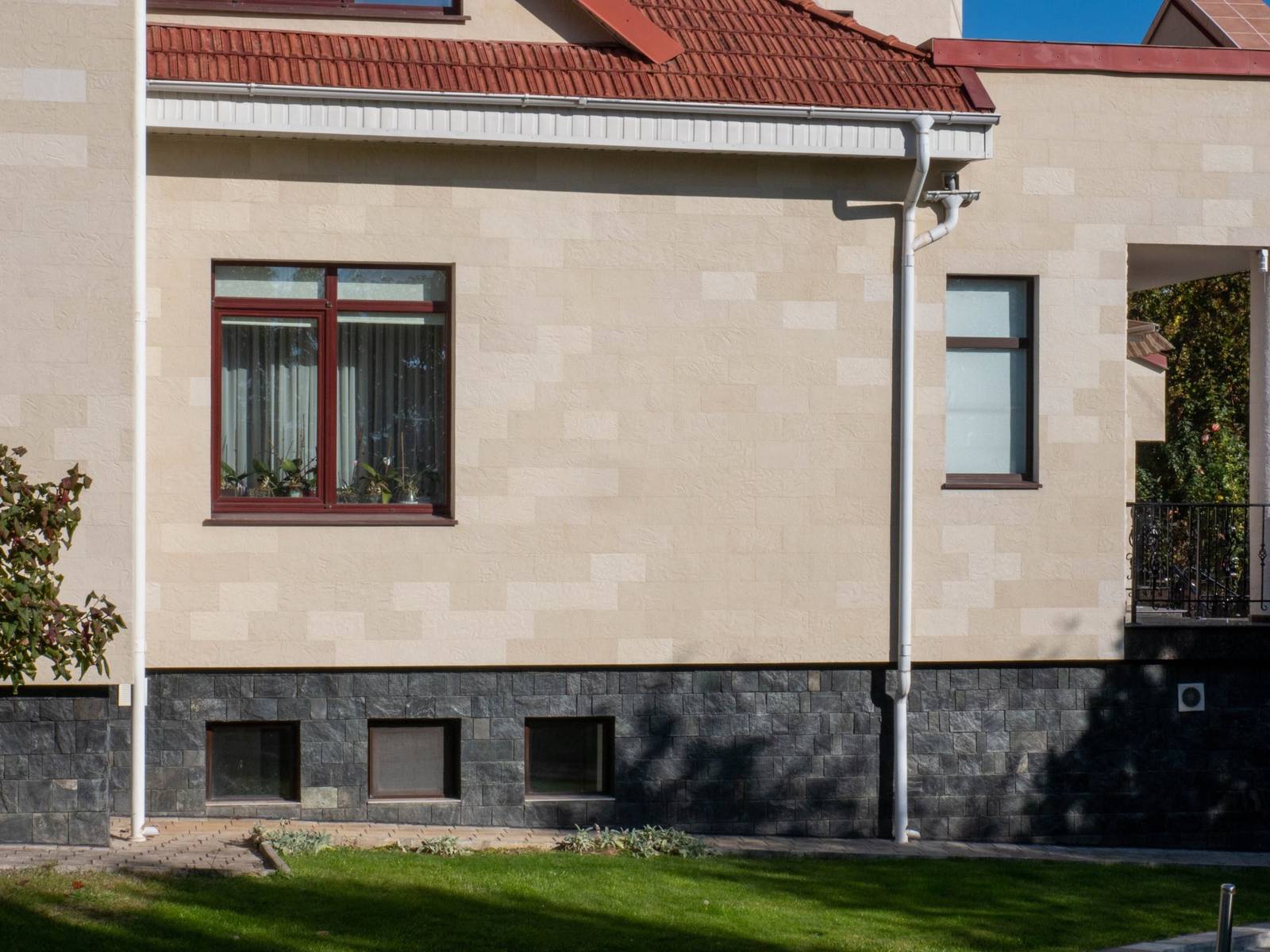 Vue latérale de la maison aux grandes fenêtres et toit rouge, habillée de pierre flexible beige