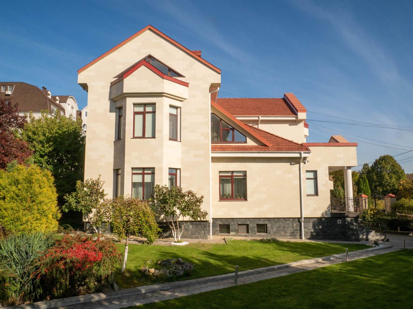 Vue latérale de la maison : hauts pignons, toit rouge et façade en pierre flexible Tender Rock, pelouse